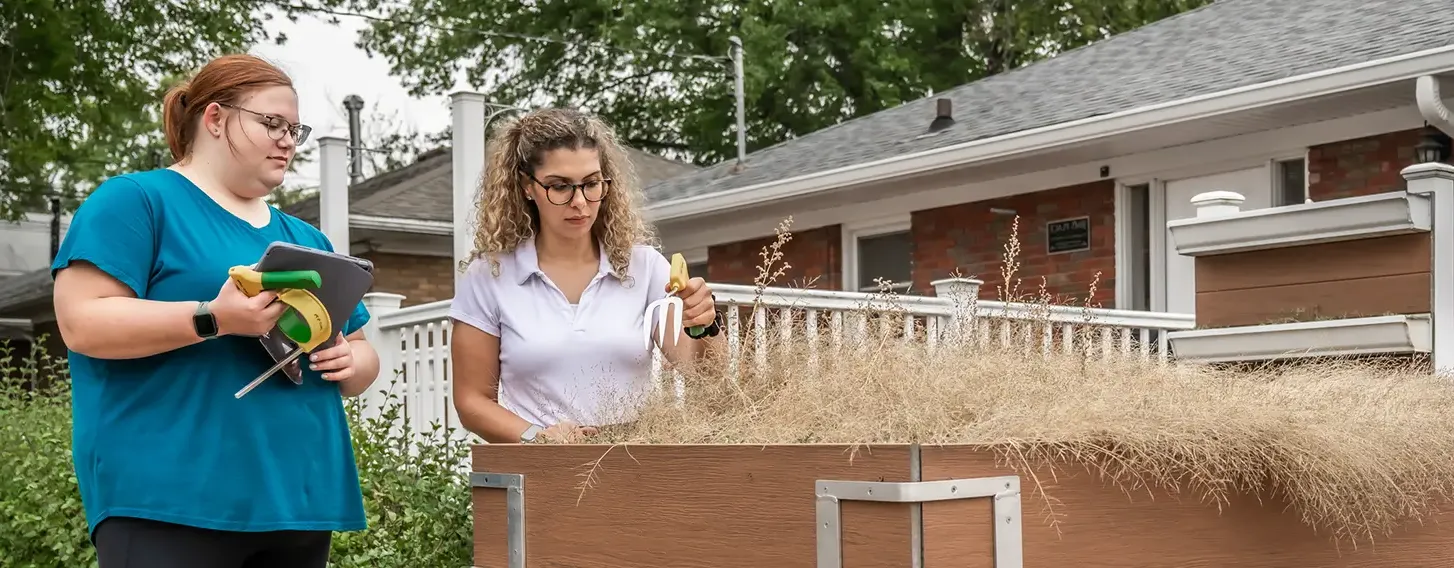 Two women working conducting an assessment outdoors next to a raised planter.